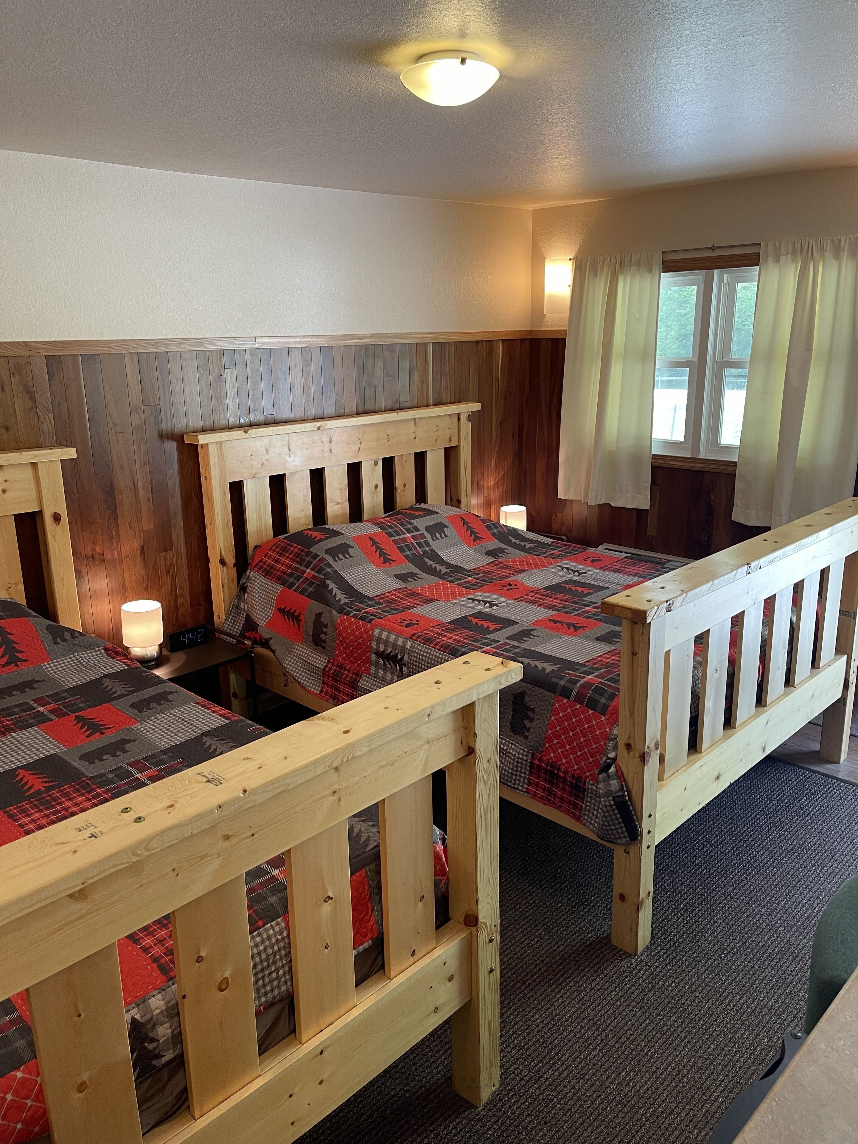 A room with two wooden beds, a wooden headboard, a clock, and a window with curtains.