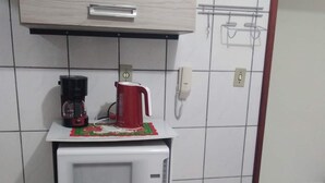 A compact kitchenette with a microwave, coffee maker, and kettle on a countertop, a small cabinet below, and a phone mounted on the wall. - Itapema - Ap. Inteiro em Itapema Rua 129 B (Centro Itapema)