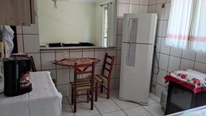 A compact kitchen with a refrigerator, a coffee maker, and a dining table with chairs. - Itapema - Ap. Inteiro em Itapema Rua 129 B (Centro Itapema)