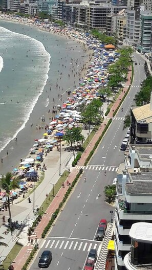 Une plage avec des parasols et des gens, une route avec des voitures, et des bâtiments en arrière-plan.
