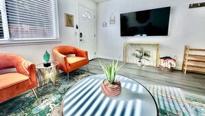 Un salon avec un canapé, un fauteuil, une table basse et un téléviseur fixé au mur.