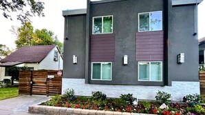 Un bâtiment moderne à deux étages, doté d’une façade grise, d’un portail en bois et d’un parterre fleuri à l’avant.