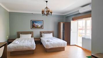 A hotel room with two beds, a wooden floor, a painting on the wall, and a window with a view.