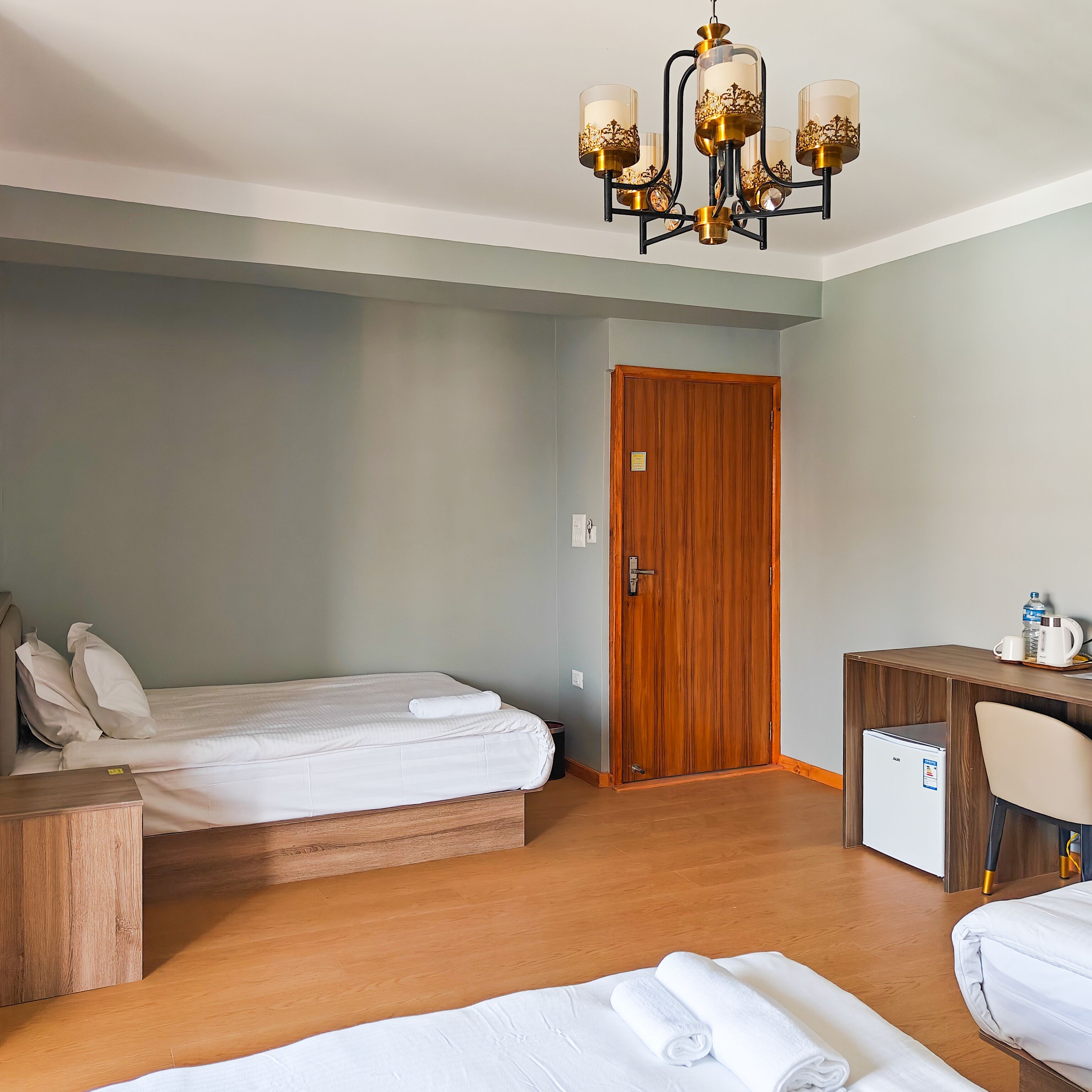 Una camera d'albergo con una scrivania in legno, un letto con lenzuola bianche, un armadio in legno e un minibar.