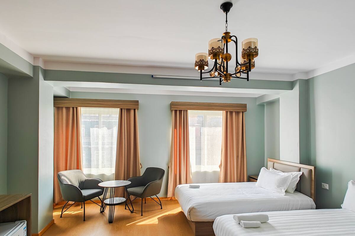 A hotel room with two beds, a small table with chairs, and a chandelier.