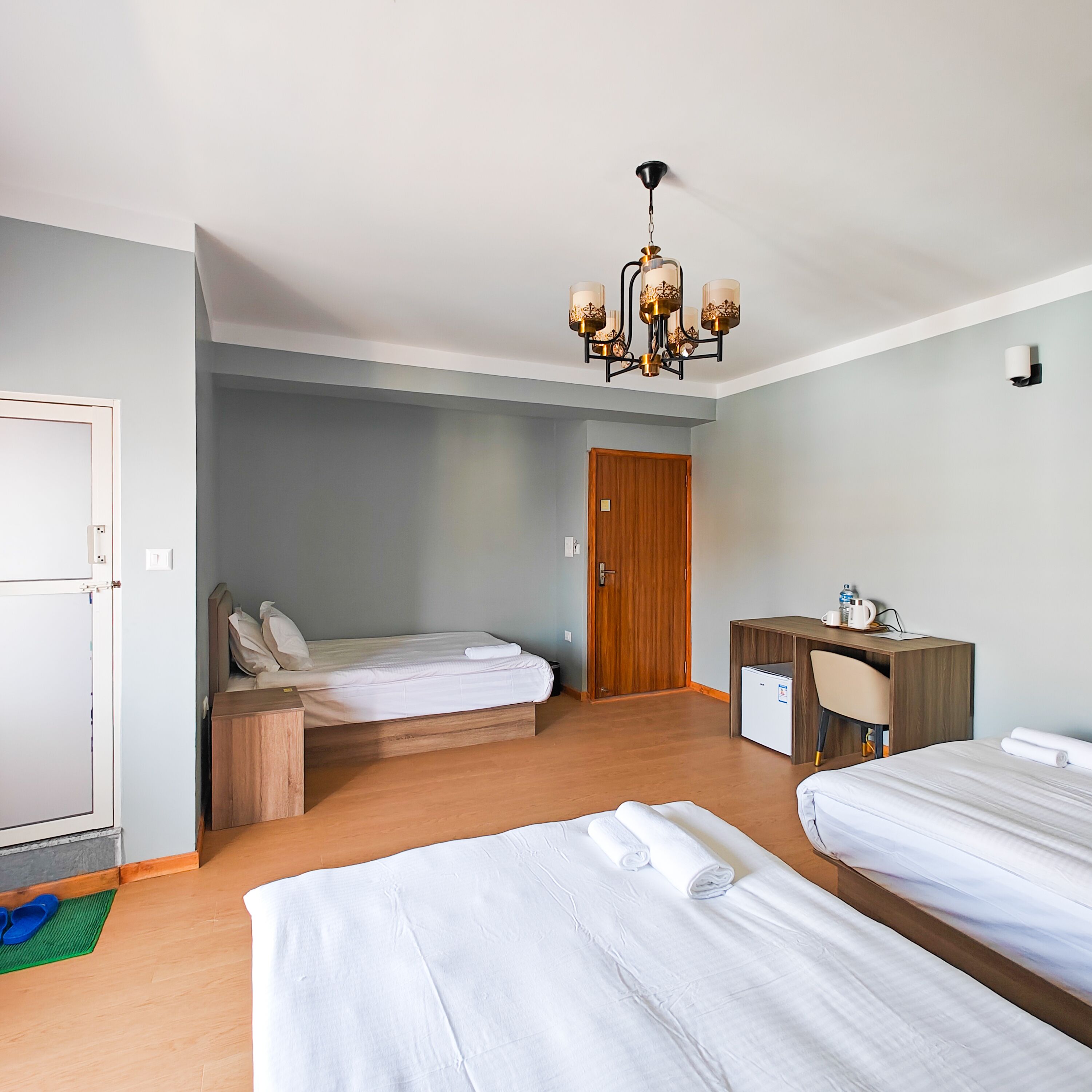 Habitación de hotel con dos camas, un escritorio de madera, un refrigerador pequeño y una araña.