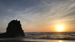 A beach with a large rock formation and the sun setting over the ocean. - Whale Watchers Bluff - Amazing Panoramic Views! (Manchester)