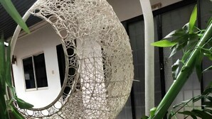A hanging chair made of white netting, surrounded by green plants and a small garden area with artificial grass. - Sea Inn Guesthouse (Sihanoukville)