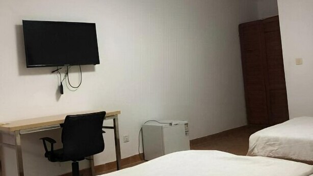 A room with two beds, a desk with a chair, a television, and a wardrobe. - Sea Inn Guesthouse (Sihanoukville)