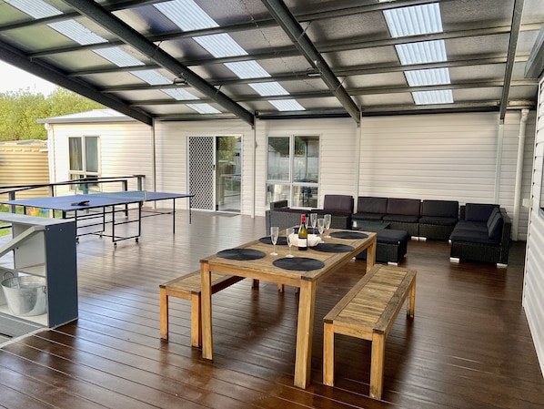 An outdoor covered patio with a ping pong table, a wooden table with wine glasses, and a black sofa. - Central convenience for groups and families - Portarlington entertainer! (Portarlington)