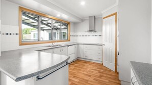 Eine moderne Küche mit weißen Schränken, einer Arbeitsplatte aus Granit, einem großen Fenster mit Blick und einem Holzboden.