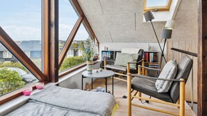 Ein gemütliches Schlafzimmer im Loft-Stil mit großem Dachfenster, einem Bett, einem Lesesessel, einem kleinen Tisch und einem Bücherregal.