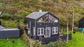 Eine zweistöckige Holzhütte mit einem steilen Dach, großen Fenstern und einer kleinen Veranda.