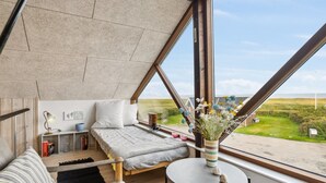 Ein modernes Schlafzimmer mit großem Fenster, einem Bett, einem kleinen Tisch und Blick auf die Landschaft.