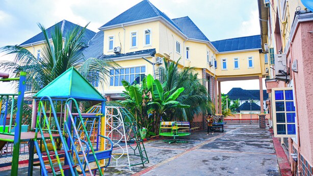 A residential area with a playground, a large yellow house with a blue roof, and a red building with a satellite dish. - 6A Resort and Hotels Owerri (Owerri)