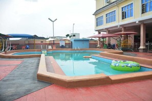 Une piscine avec un toboggan, un petit espace de jeux et un bĂątiment dotĂ© de grandes fenĂȘtres.
