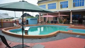 A swimming pool with lounge chairs and umbrellas, a covered area with a play structure, and a building with multiple windows. - 6A Resort and Hotels Owerri (Owerri)