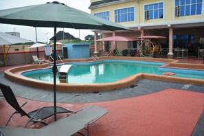 A swimming pool with lounge chairs and umbrellas, a covered area with a play structure, and a building with multiple windows.
