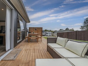 Een houten terras met een bank en tafel, een houten schutting en een voertuig op de achtergrond.
