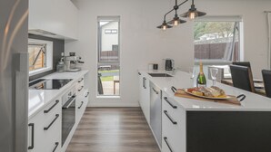 A modern kitchen with white cabinetry, a built-in oven, and a large island with a wooden countertop. - A Sunshine Retreat - Pauanui Holiday Home (Pauanui)