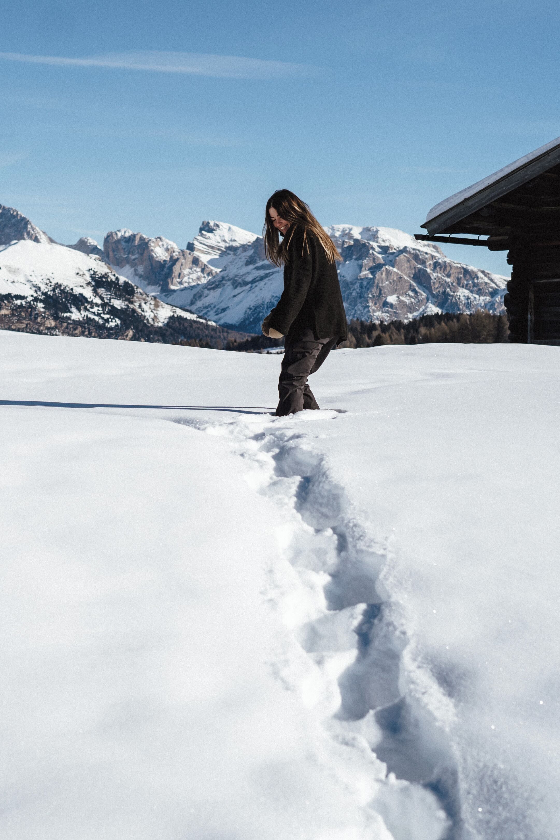 A person walking on snow-covered ground with mountains in the background.