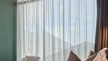 A hotel room with a bed, pillows, and a window with sheer curtains.