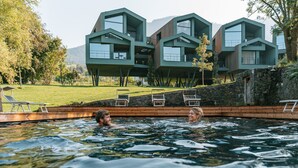 A swimming pool with two people in the water, surrounded by modern buildings with balconies. - FLORIS GREEN SUITES (Castelrotto)