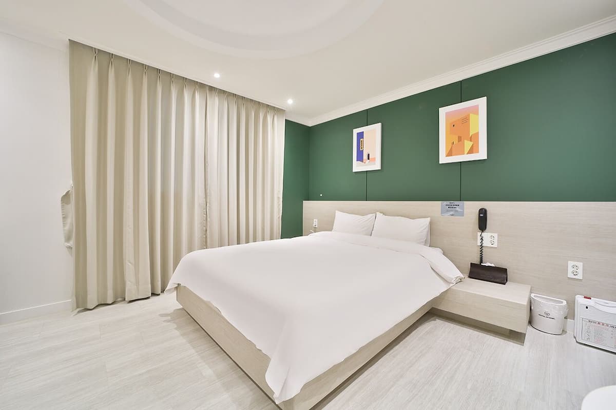 A hotel room with a large bed, a bedside table, a telephone, and a waste bin.