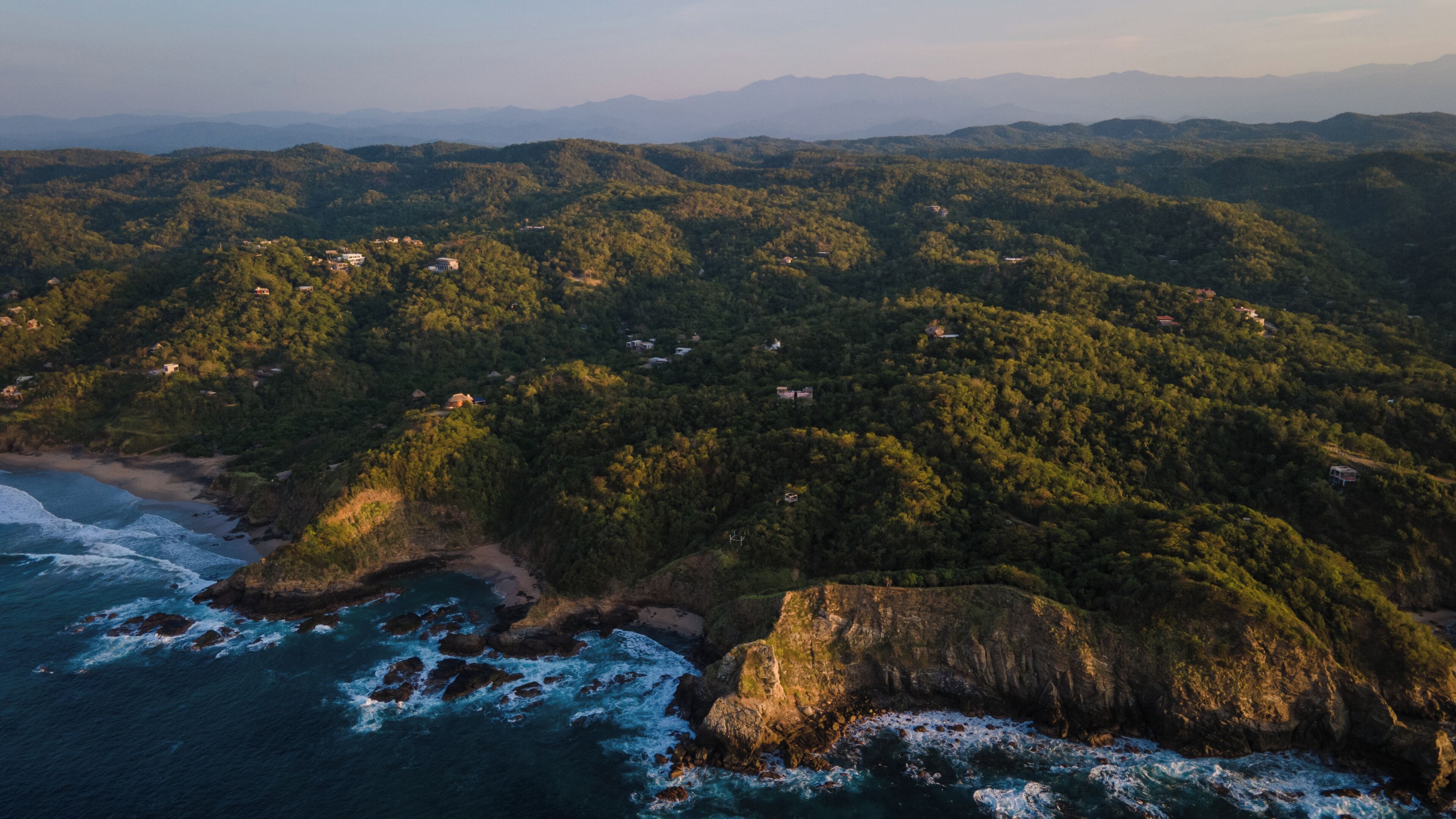 A coastal landscape with dense forest, rocky coastline, and scattered buildings.