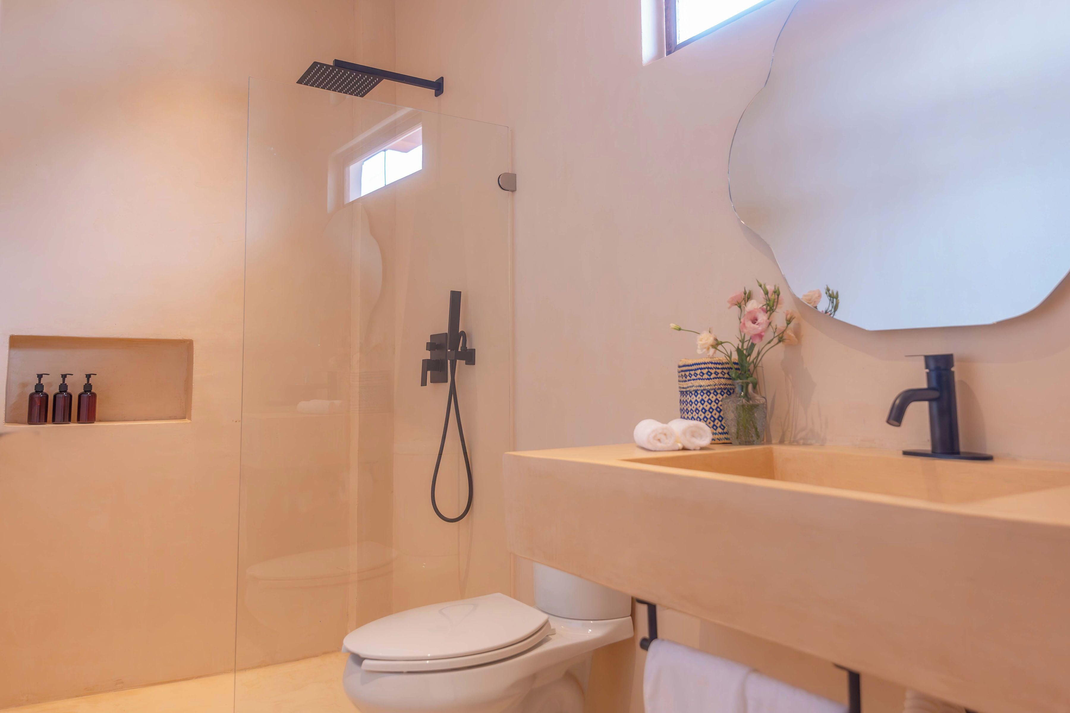 A modern bathroom with a glass-enclosed shower, a white toilet, a wooden vanity with a sink, and a mirror.
