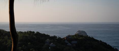 A coastal view with a house on a hill overlooking the sea.