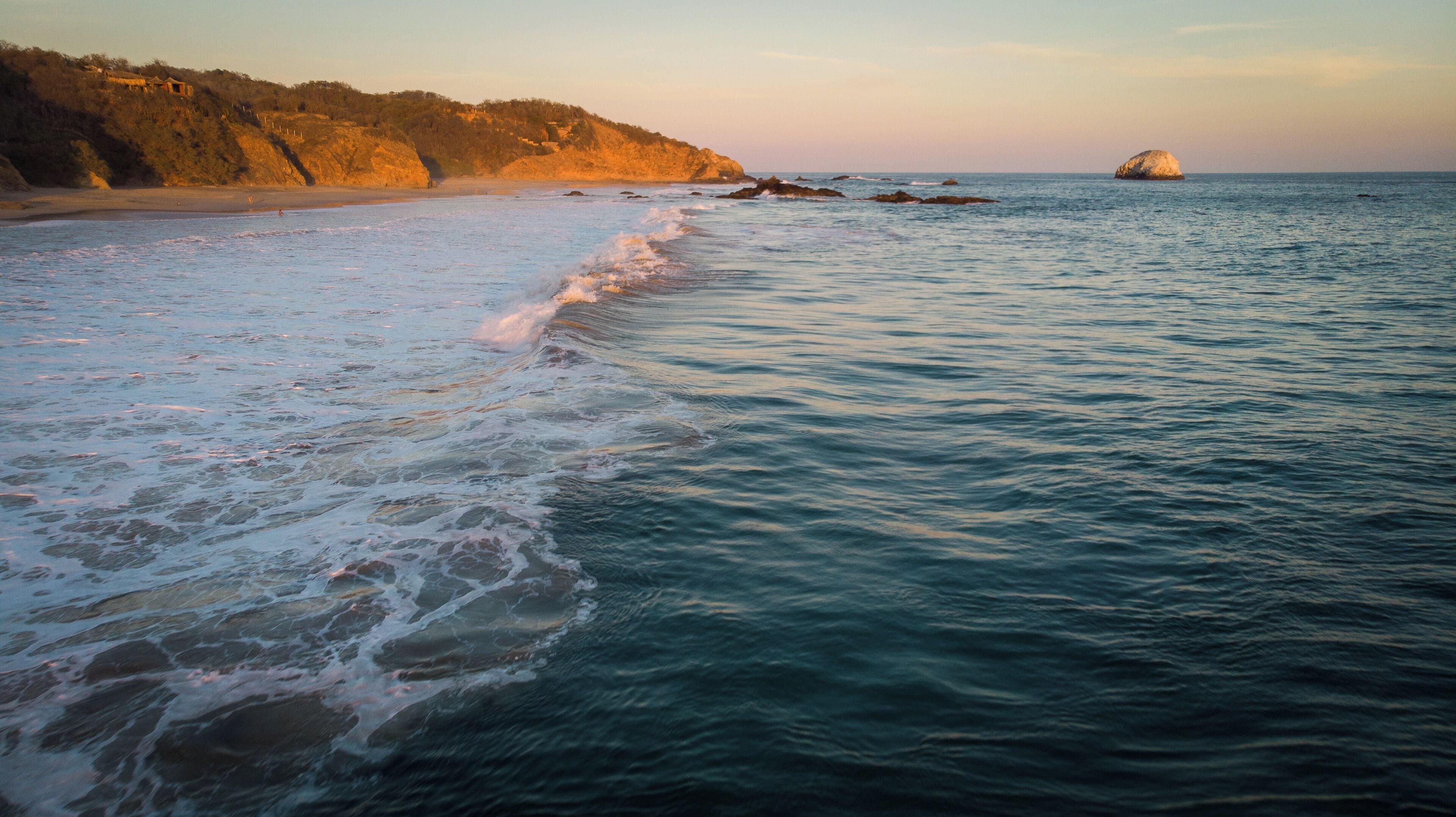 A beach with waves, a rocky outcrop, and a distant island.