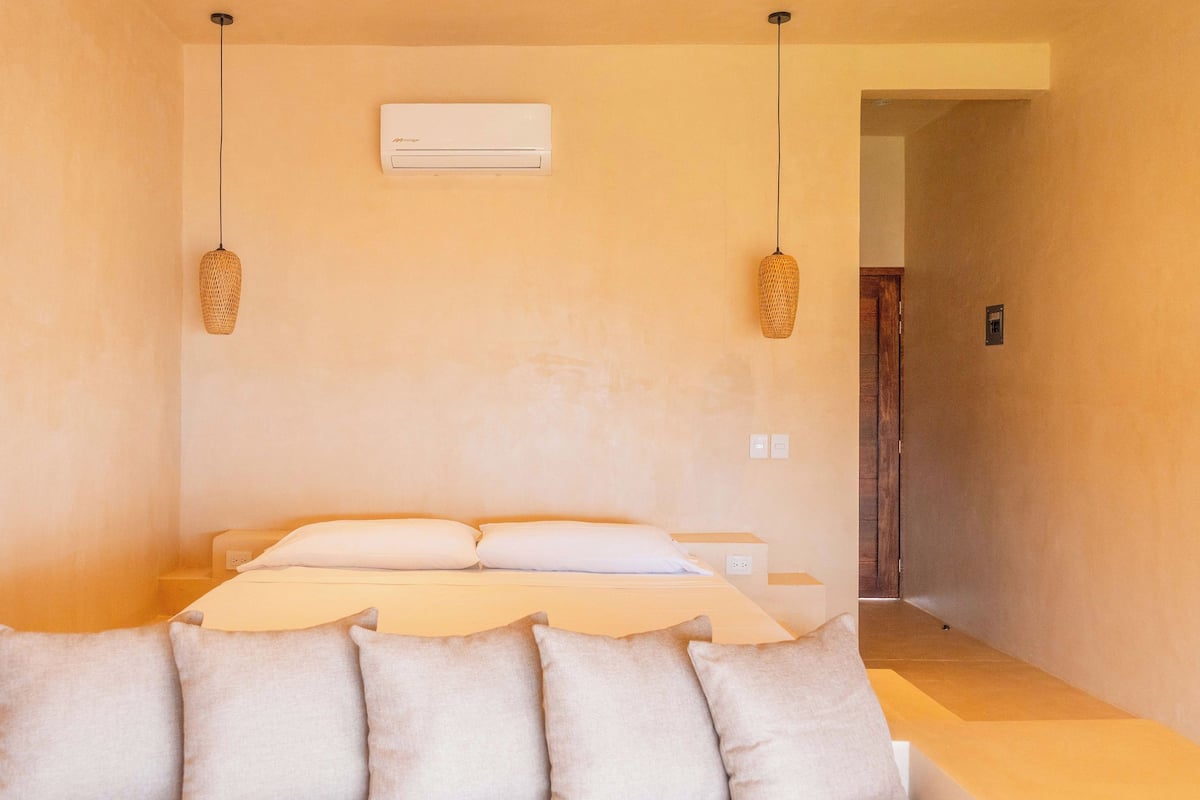 Un dormitorio con una cama, dos lámparas colgantes, un equipo de aire acondicionado y una puerta que da a otra habitación.