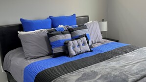 A neatly made bed with a grey and blue bedspread, multiple pillows in shades of grey, blue, and black, and a black headboard. - 🌻Sunflower Cottage🌻Breathtaking Mountain Views & Fresh Air Retreat! (Flagstaff)
