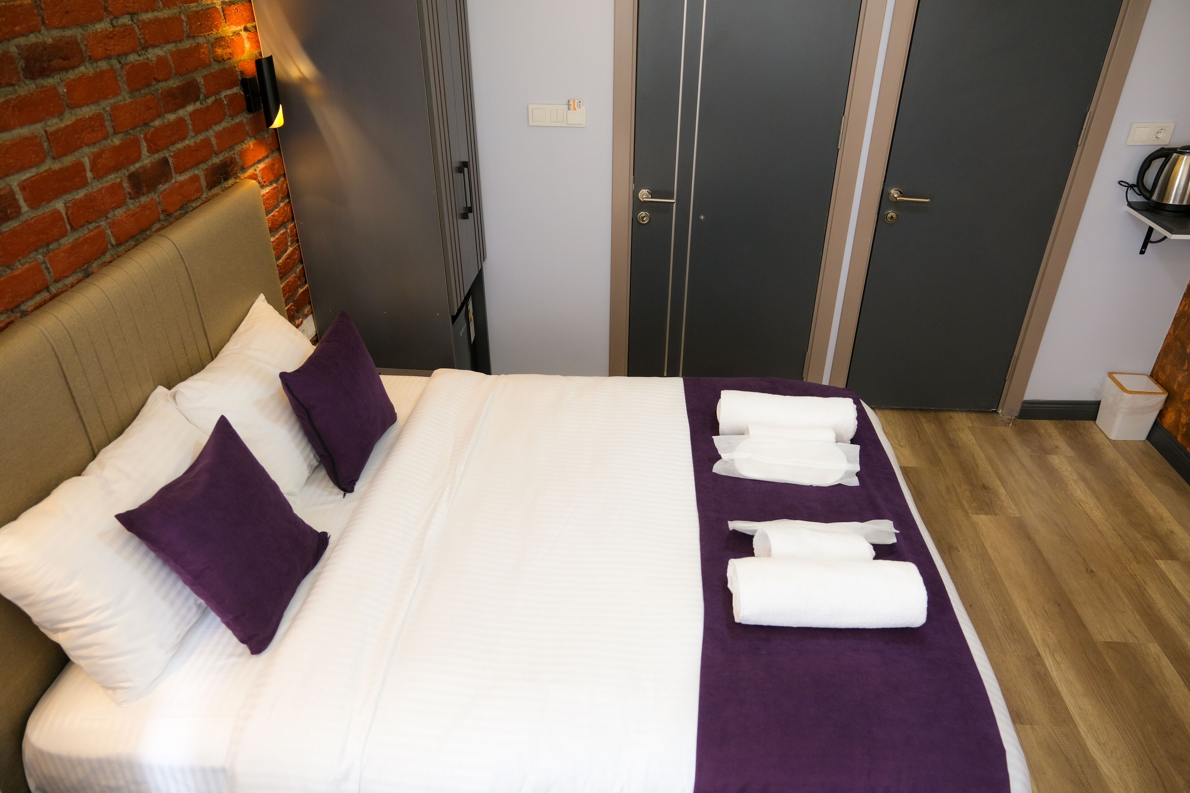 A hotel room with a bed, pillows, a purple blanket, and towels.