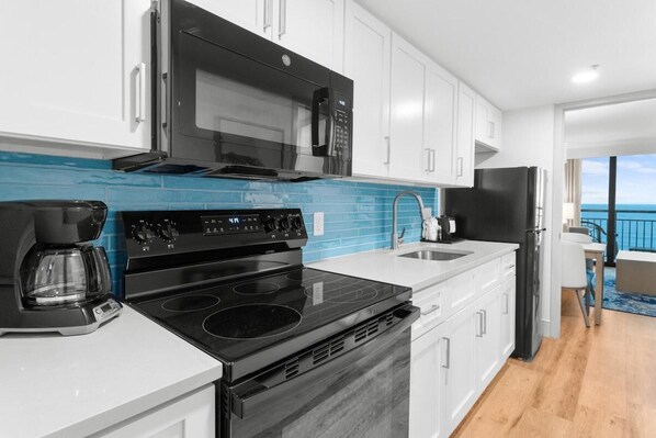 A modern kitchen with a black stove, white cabinets, and a blue backsplash. - Adventures: 10th Floor With a View of the Ocean (Myrtle Beach)