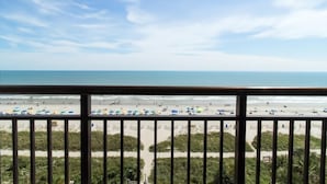 Vista a la playa desde un balcón con barandilla, playa de arena y océano.