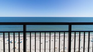 Une vue sur la plage depuis un balcon doté d’une balustrade, avec une plage de sable et l’océan en toile de fond.