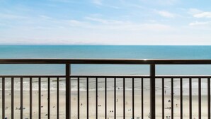 Uitzicht op een strand vanaf een balkon met een leuning, heldere lucht en een kalme zee.