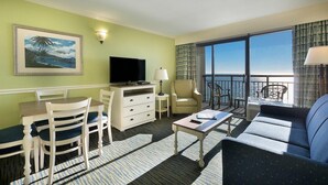 A hotel room with a balcony, a television, a dining area with chairs and a table, and a sofa. - Low Floor Oceanfront Suite: Your Crew's Getaway (Myrtle Beach)