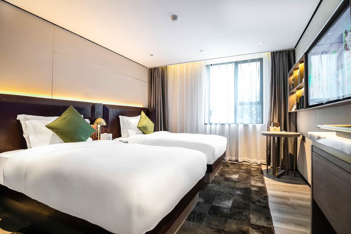 Une chambre d’hôtel avec deux lits, une télévision, une petite table et une grande fenêtre avec des rideaux.