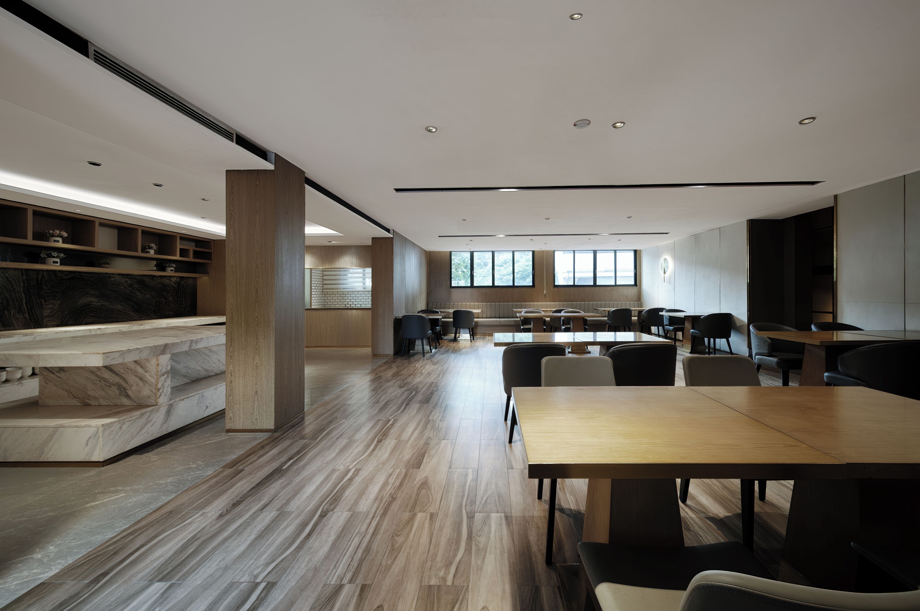 A modern interior with a marble reception desk, wooden flooring, and a dining area with tables and chairs.