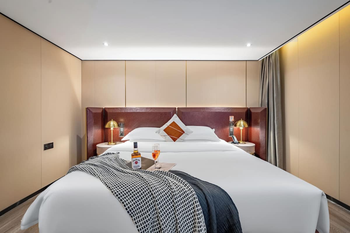 Une chambre d’hôtel avec un grand lit, deux tables de chevet avec des lampes, un minibar et une vue sur la ville.