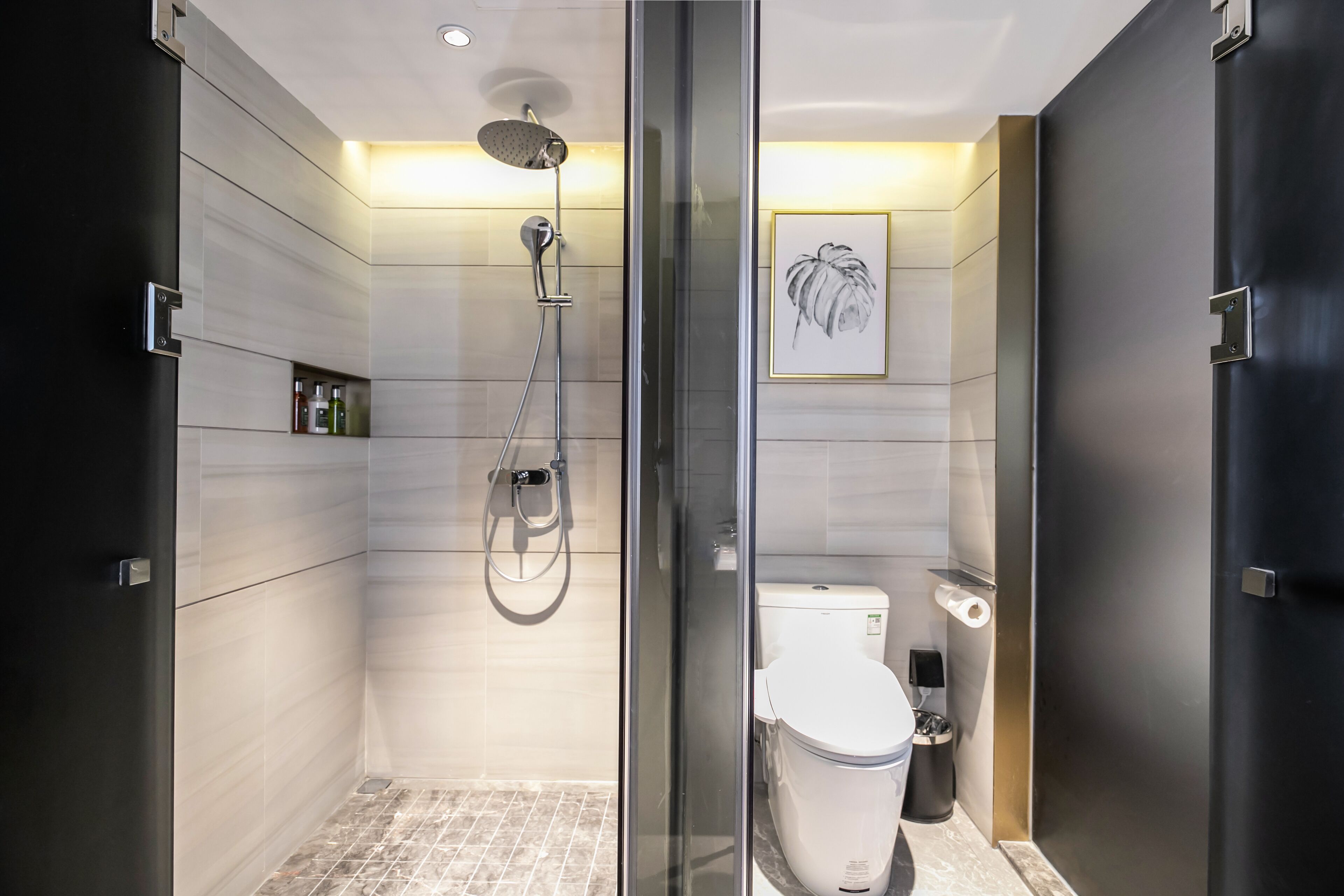 A modern bathroom with a glass-enclosed shower, a toilet, and a framed artwork on the wall.