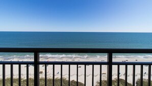 A beach view from a balcony with a railing, sandy beach, and ocean. - Elevated Elegance: Deluxe One Bedroom King Suite (Myrtle Beach)
