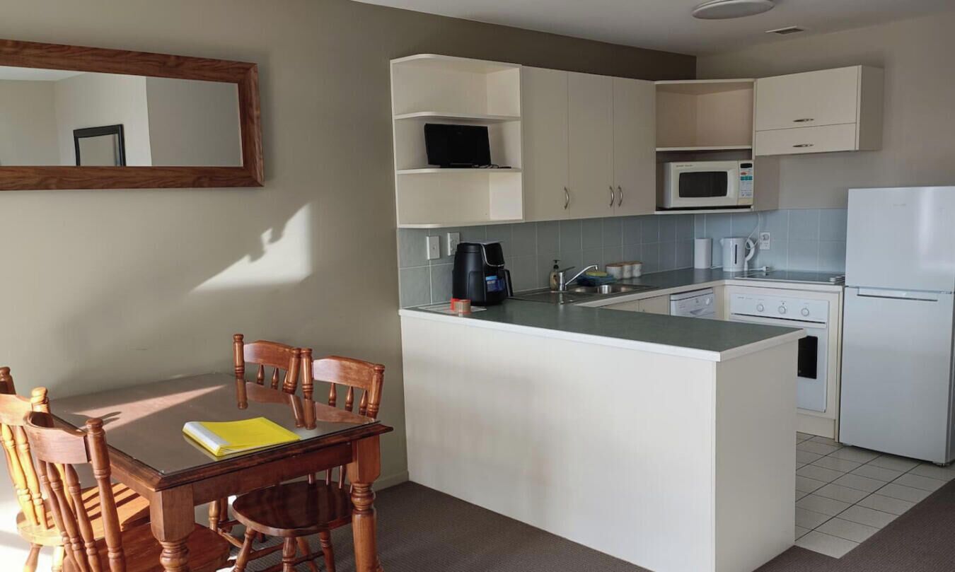 Una cocina compacta con una isla central, muebles blancos, microondas, cafetera y refrigerador.