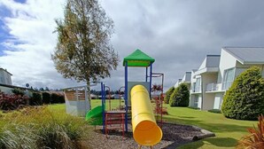 A playground with a yellow slide, surrounded by grass and a few trees. - Opuke Crash Pad Methven - with mountain views. (Methven)