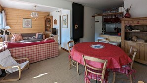 Ein gemütliches Zimmer mit einer Couch, einem Esstisch mit Stühlen, einer Küchenzeile und einer Holzbalkendecke.
