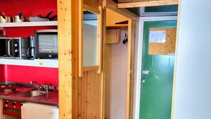 Cocina compacta con microondas, estufa y lavamanos. Se observa una puerta verde con cerradura de llave.