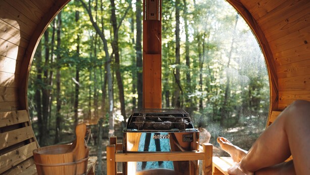 Une cabane en bois dotée d’une fenêtre circulaire, d’un sauna Harvia et d’un banc en bois.
